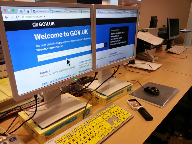 James desk set up with two monitors side by side with the screen spilt across them, a high visibility keyboard and magnifying glass