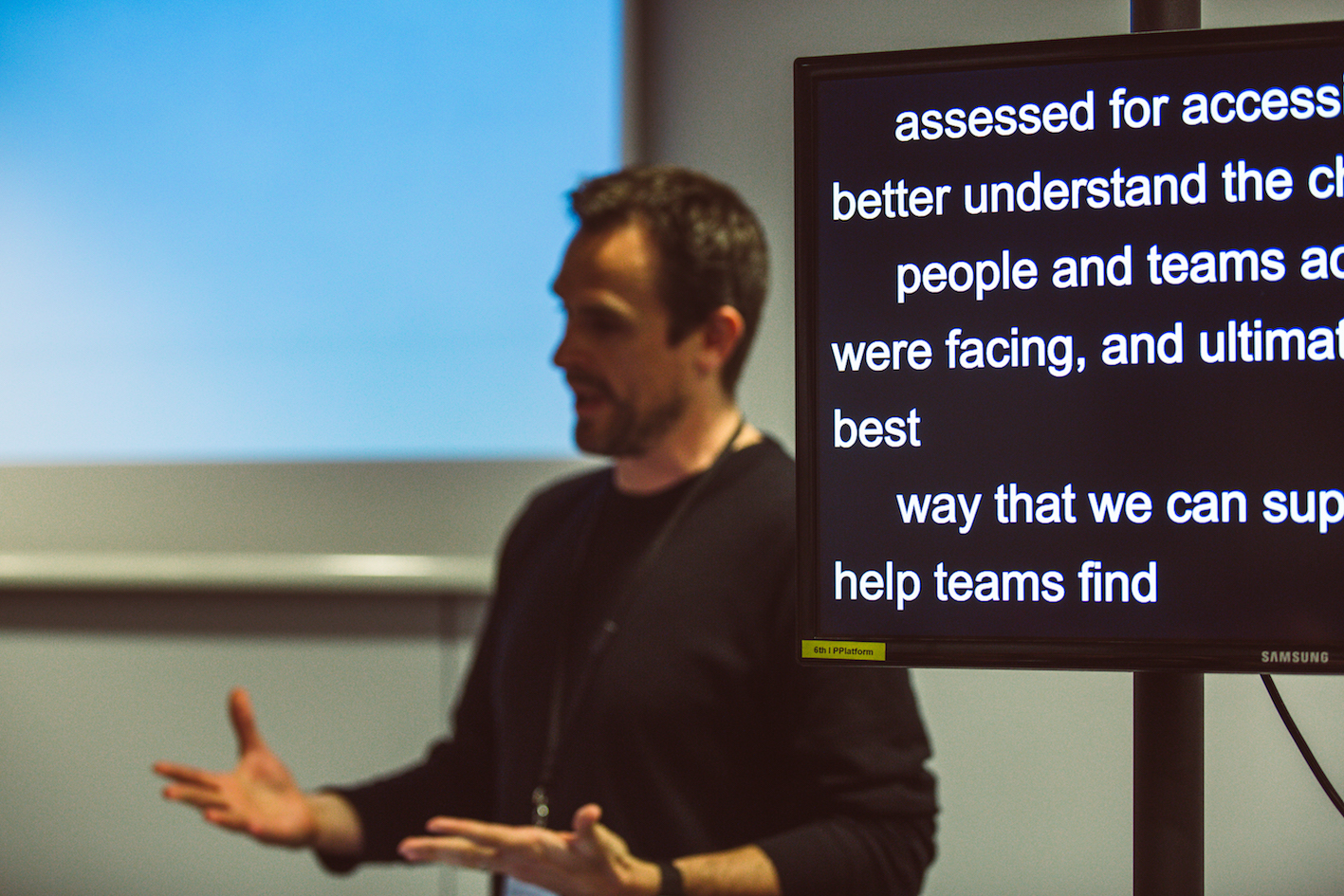 Alistair talking while a screen shows live-caption text of his presentation