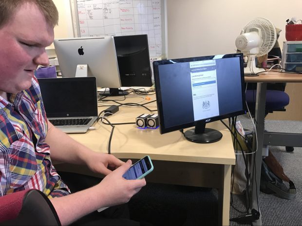 A photo of Mike using the autocomplete on an iPhone. There is a monitor nearby that mirrors the screen that Mike is using.