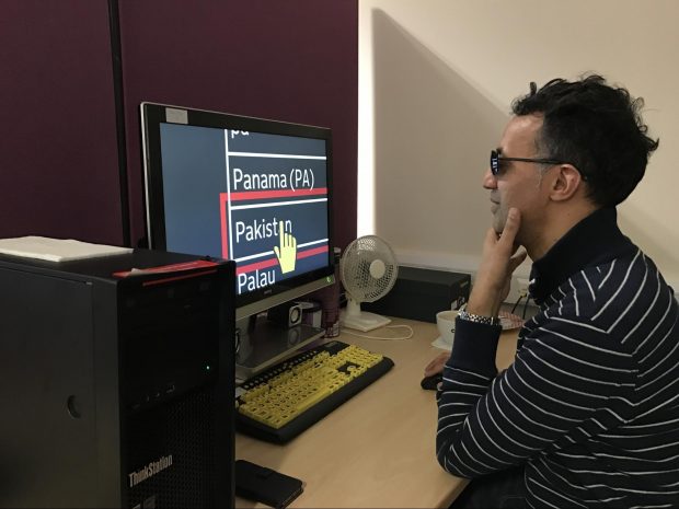 A photo of Ziad using the autocomplete. He is sat in front of a large monitor. The monitor is zoomed 12x and is using inverted colours. On screen, two options are shown, and the mouse hovers over one of them, ready to select it.