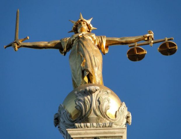 Gold statue Of 'Justice', Central Criminal Court, Old Bailey, London viewed from a low angle against a blue sky.