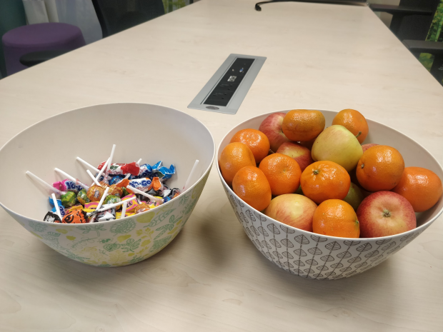 2 colourful bowls on a desk containing fruits (apples and satsumas) and sweets