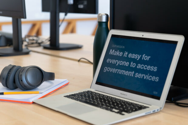 Image of a laptop with the text 'Make it easy for everyone to access government services' on the screen next to a set of headphones and notebook