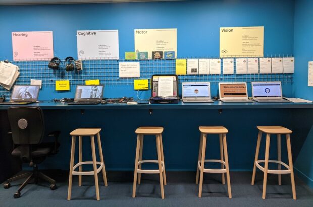 A room filled with various devices and assistive technology on display. Accessibility posters are visible on the walls, showcasing information and resources. The devices include a mix of tools designed to support accessibility needs.